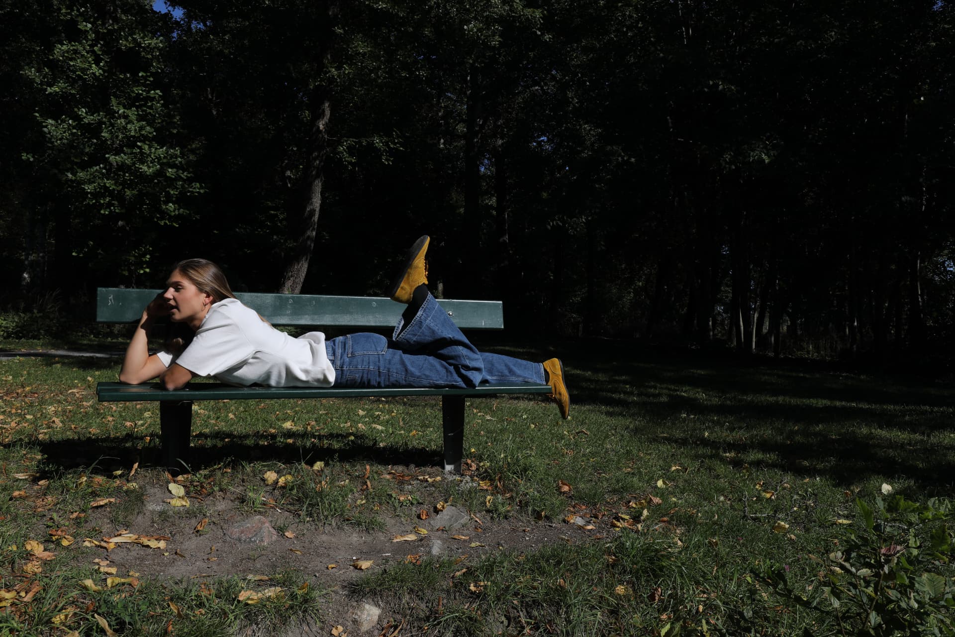 Woman lying on a green park bench in a sunlit clearing